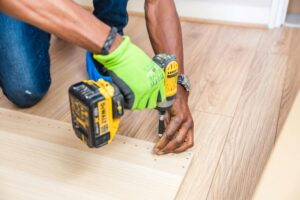 Close-up of handyman drilling wood indoors with green gloves and cordless drill.