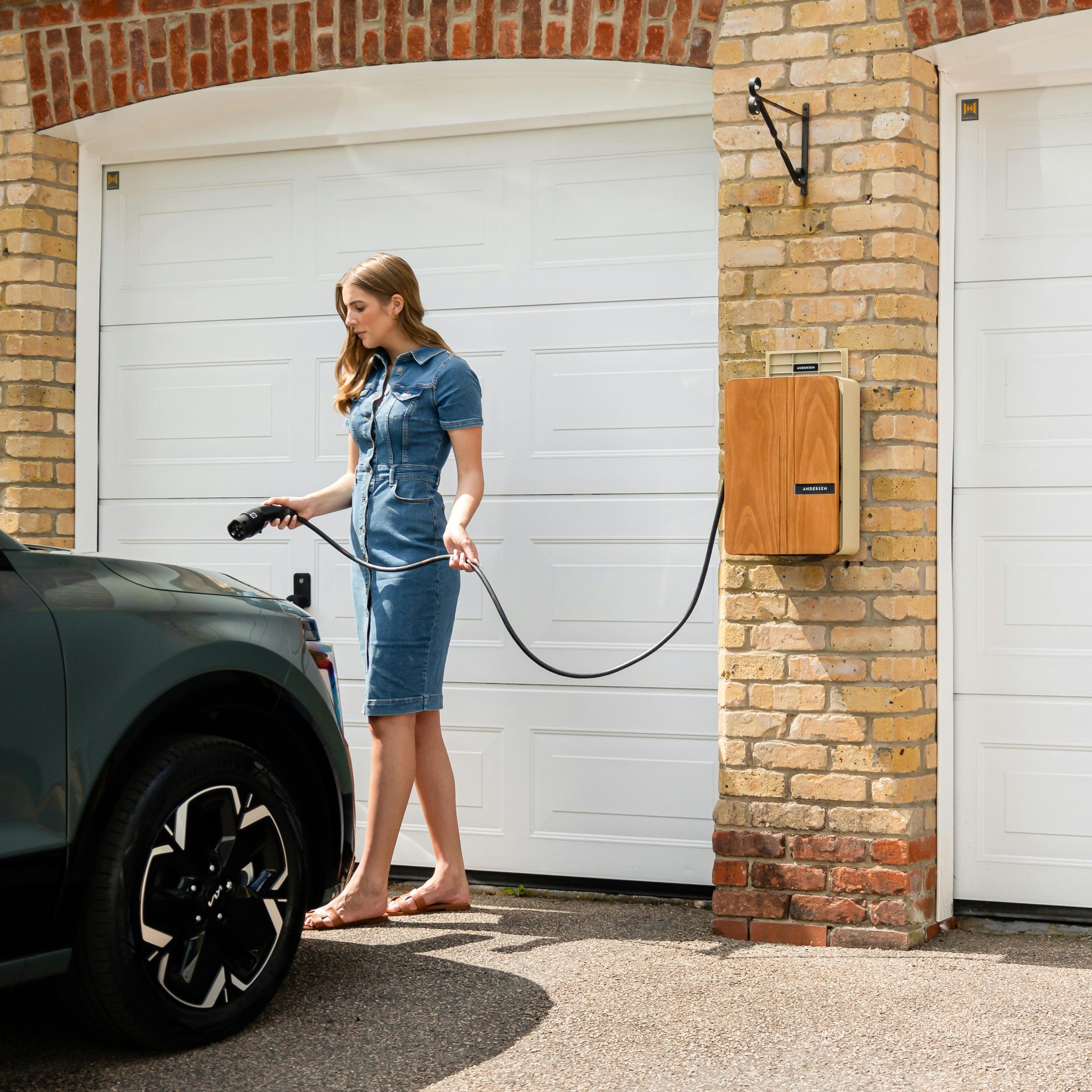 A woman connects her electric car to a home charging station in a residential garage.