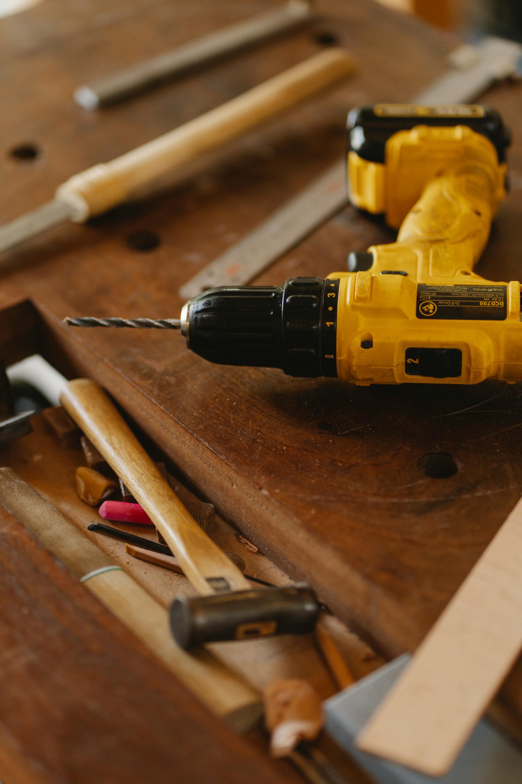 From above of contemporary screwdriver with drill near hammer and tools on wooden desk