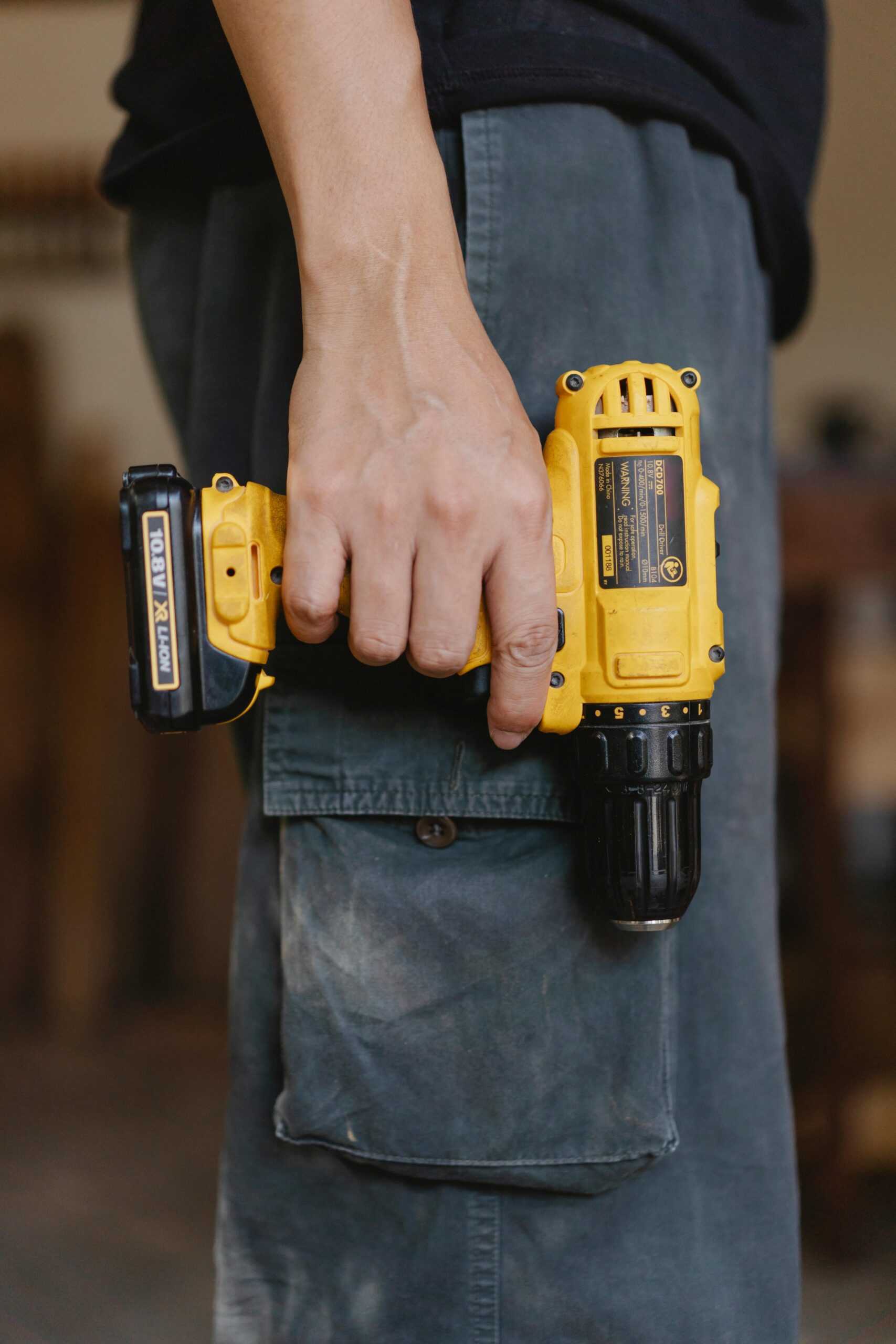 Side view of unrecognizable craftsman in casual clothes standing with electric cordless screwdriver in workshop