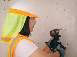 Female worker in safety gear drilling into a wall. Demonstrating adherence to safety standards on a construction site.